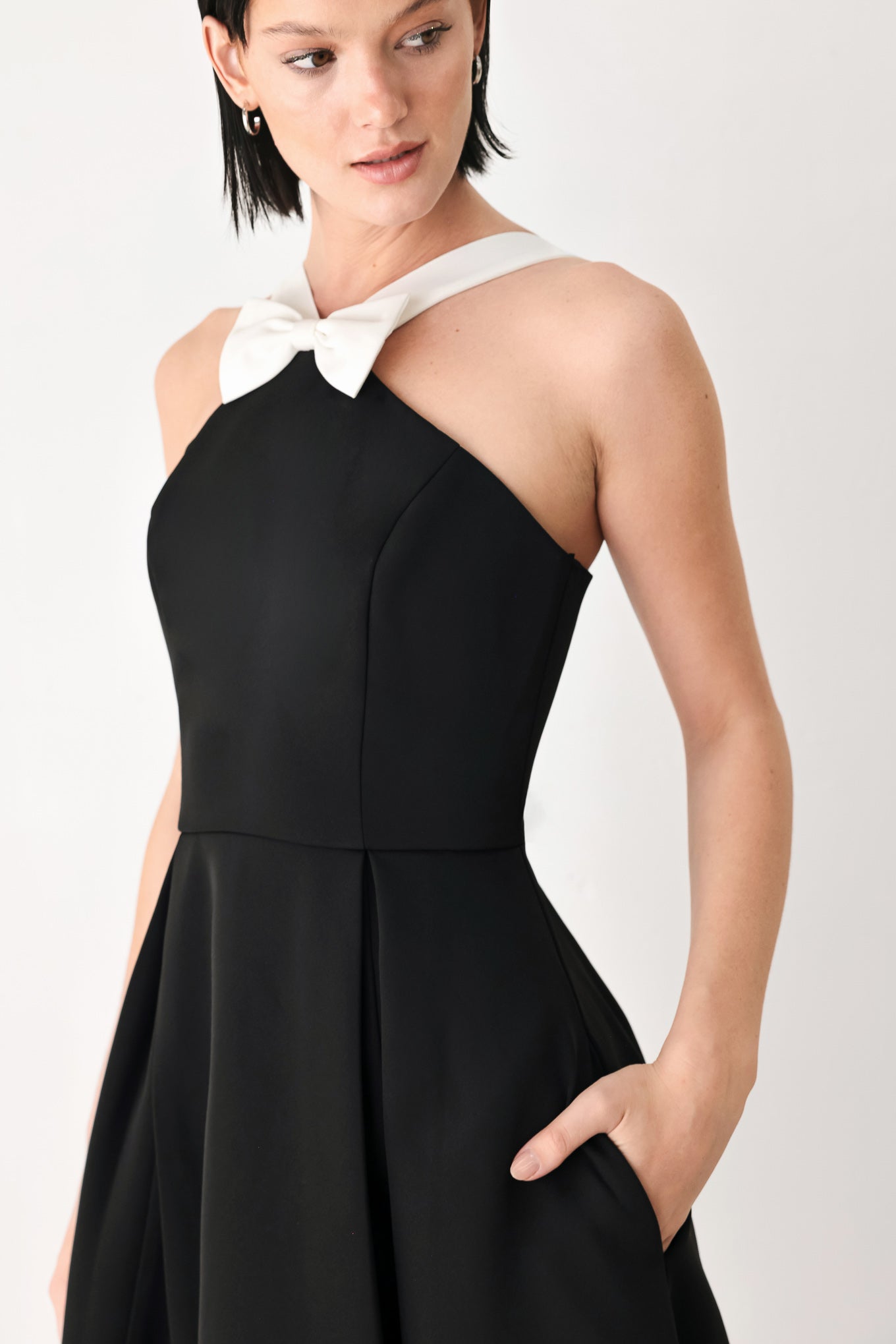 A woman modeling a black halter midi dress with a contrasting white bow at the neckline | FREEMARKET