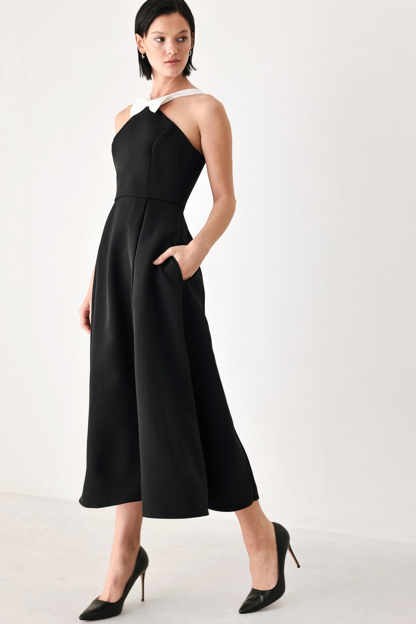 A woman modeling a black halter midi dress with a contrasting white bow at the neckline | FREEMARKET