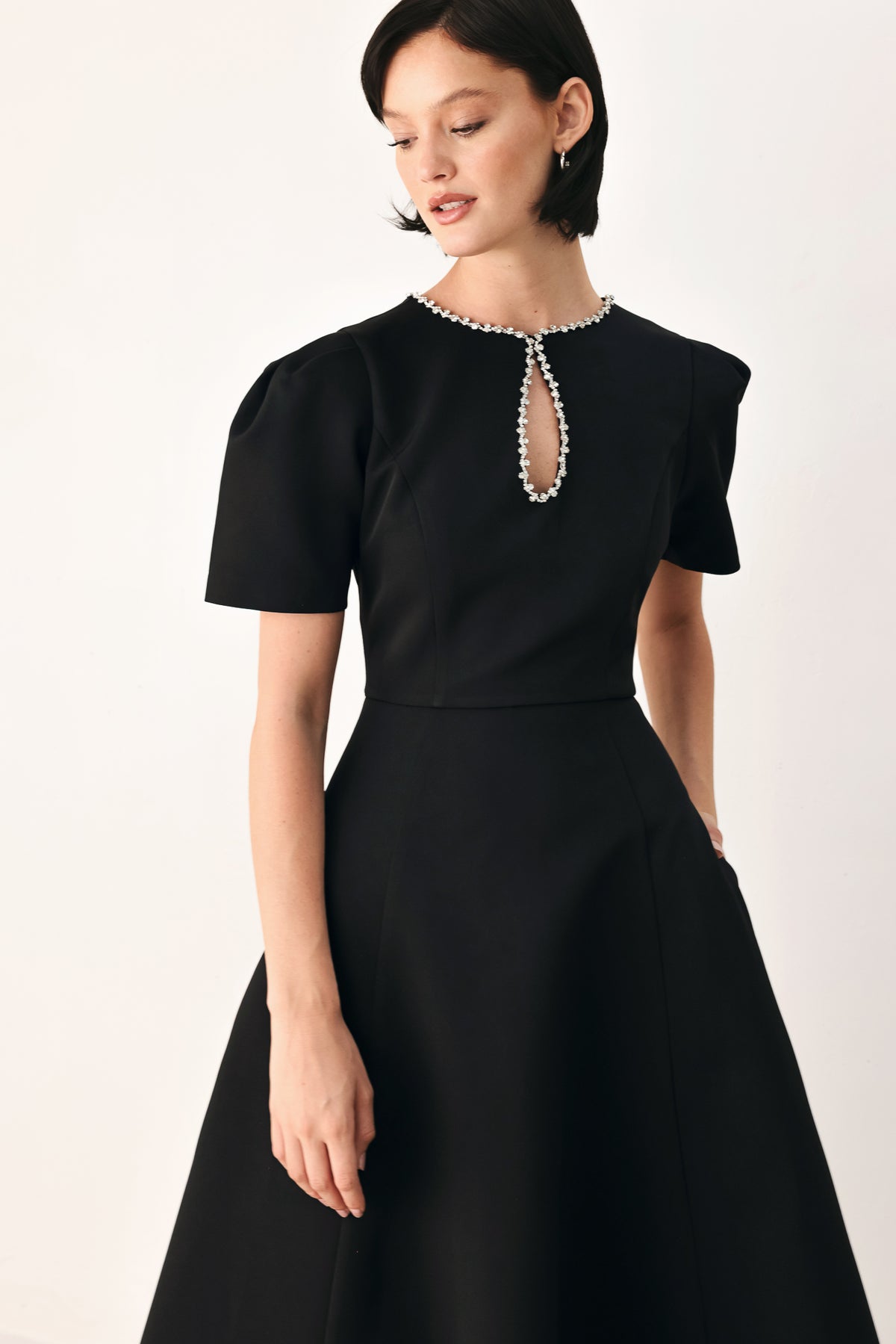 A woman modeling a black midi dress with short puff sleeves, a keyhole neckline with rhinestone embellishments, and a flared skirt | FREEMARKET