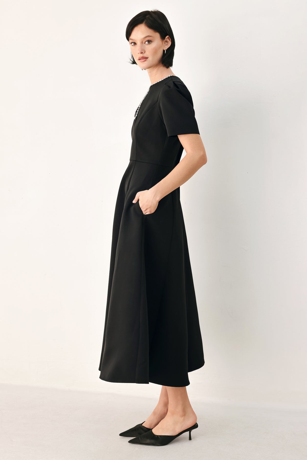 A woman modeling a black midi dress with short puff sleeves, a keyhole neckline with rhinestone embellishments, and a flared skirt | FREEMARKET