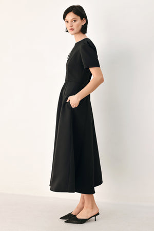 A woman modeling a black midi dress with short puff sleeves, a keyhole neckline with rhinestone embellishments, and a flared skirt | FREEMARKET