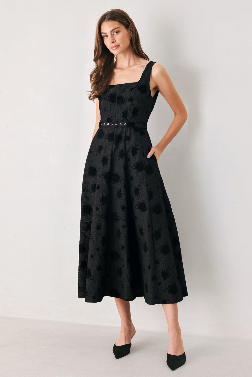 Woman wearing a sleeveless, square neckline black midid dress with jacquard floral pattern and slim waist belt | FREEMARKET 