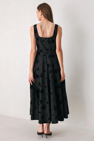 Woman wearing a sleeveless, square neckline black midid dress with jacquard floral pattern and slim waist belt | FREEMARKET 