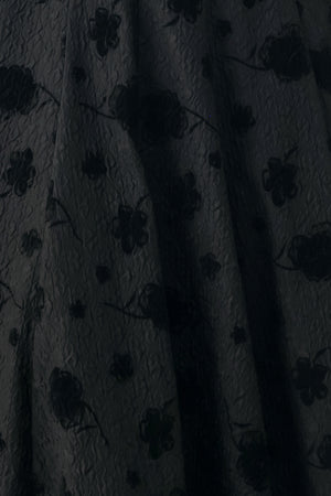 Woman wearing a sleeveless, square neckline black midid dress with jacquard floral pattern and slim waist belt | FREEMARKET 