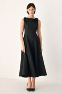 A woman modeling a sleeveless black midi dress with a boat neckline and large bow details on the shoulders | FREEMARKET
