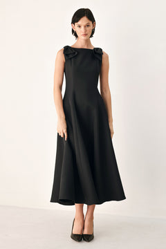 A woman modeling a sleeveless black midi dress with a boat neckline and large bow details on the shoulders | FREEMARKET
