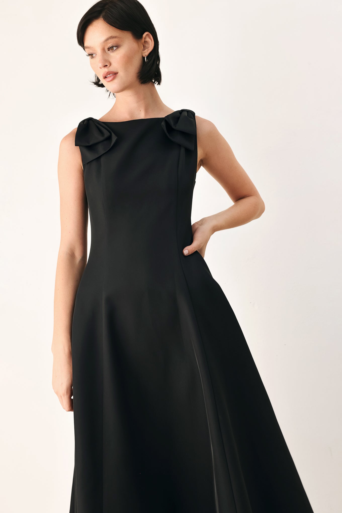 A woman modeling a sleeveless black midi dress with a boat neckline and large bow details on the shoulders | FREEMARKET