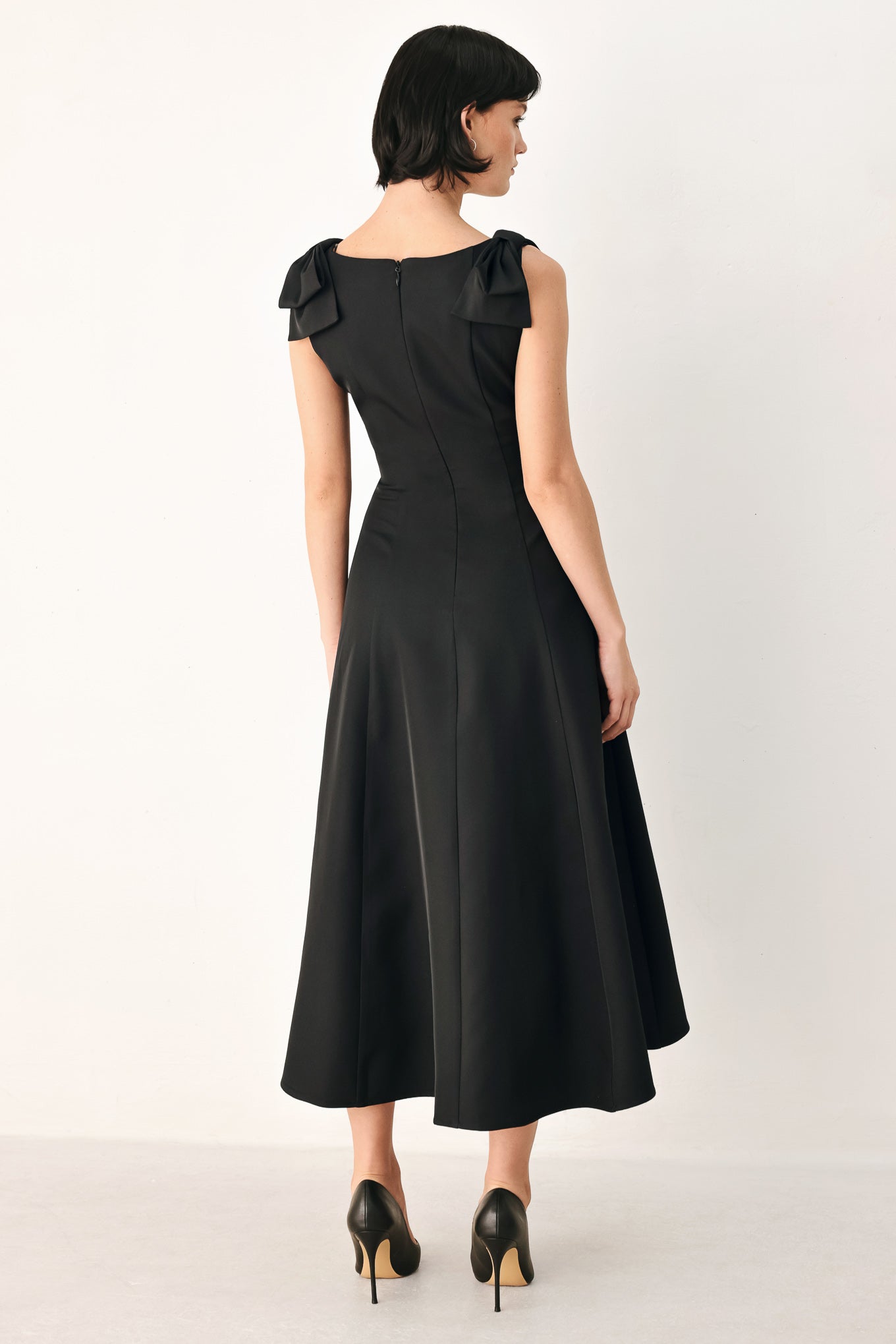 A woman modeling a sleeveless black midi dress with a boat neckline and large bow details on the shoulders | FREEMARKET