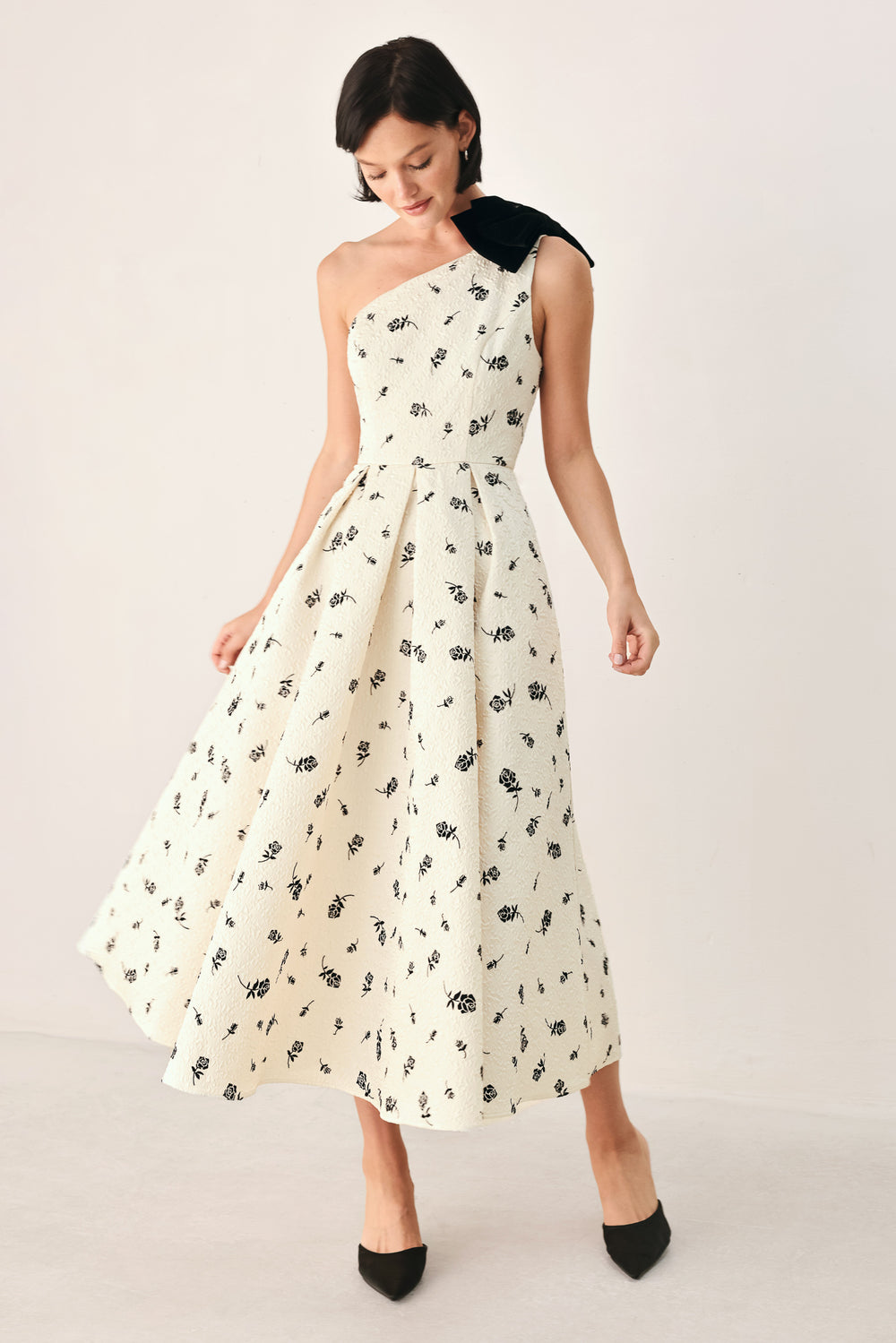 A woman models a one-shoulder midi dress with a black floral print on an off-white background, featuring a black fabric bow at the neckline | FREEMARKET