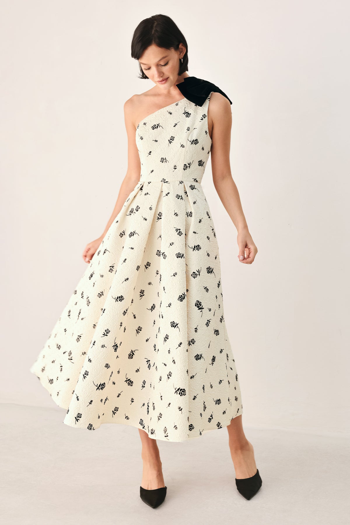 A woman models a one-shoulder midi dress with a black floral print on an off-white background, featuring a black fabric bow at the neckline | FREEMARKET