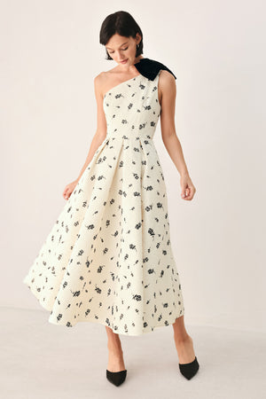 A woman models a one-shoulder midi dress with a black floral print on an off-white background, featuring a black fabric bow at the neckline | FREEMARKET