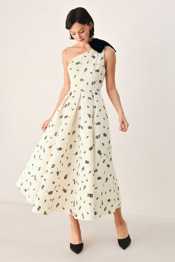 A woman models a one-shoulder midi dress with a black floral print on an off-white background, featuring a black fabric bow at the neckline | FREEMARKET