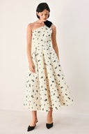 A woman models a one-shoulder midi dress with a black floral print on an off-white background, featuring a black fabric bow at the neckline | FREEMARKET
