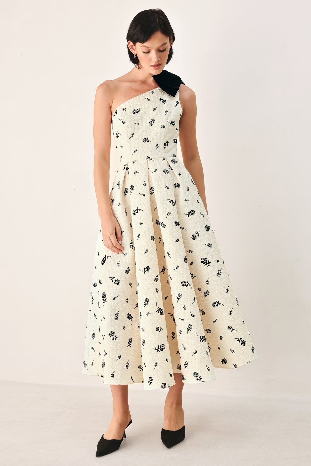 A woman models a one-shoulder midi dress with a black floral print on an off-white background, featuring a black fabric bow at the neckline | FREEMARKET