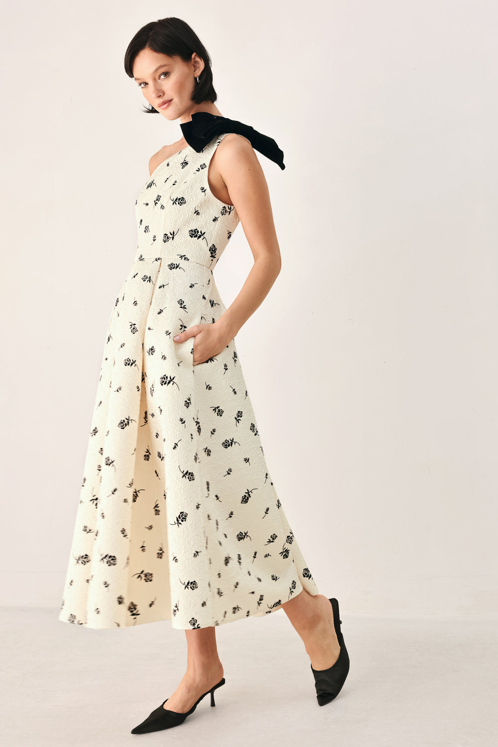 A woman models a one-shoulder midi dress with a black floral print on an off-white background, featuring a black fabric bow at the neckline | FREEMARKET