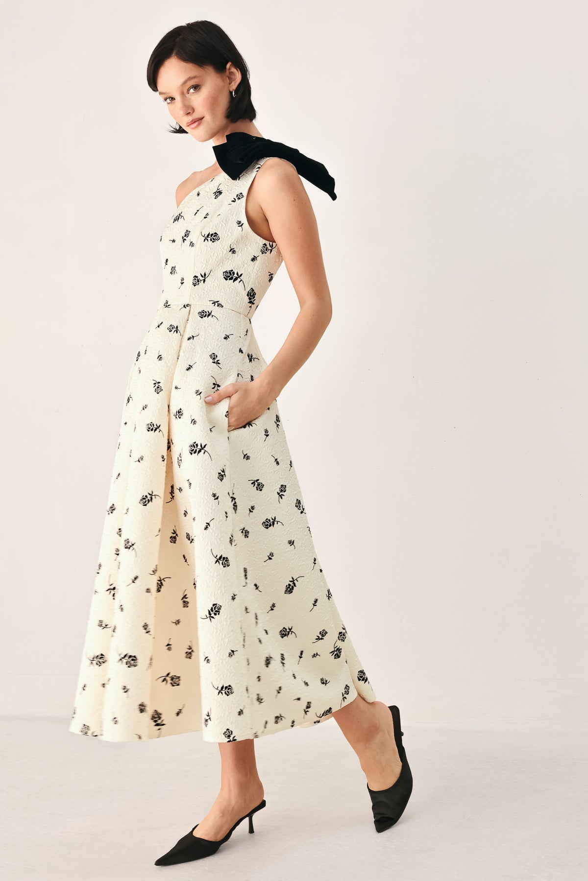 A woman models a one-shoulder midi dress with a black floral print on an off-white background, featuring a black fabric bow at the neckline | FREEMARKET