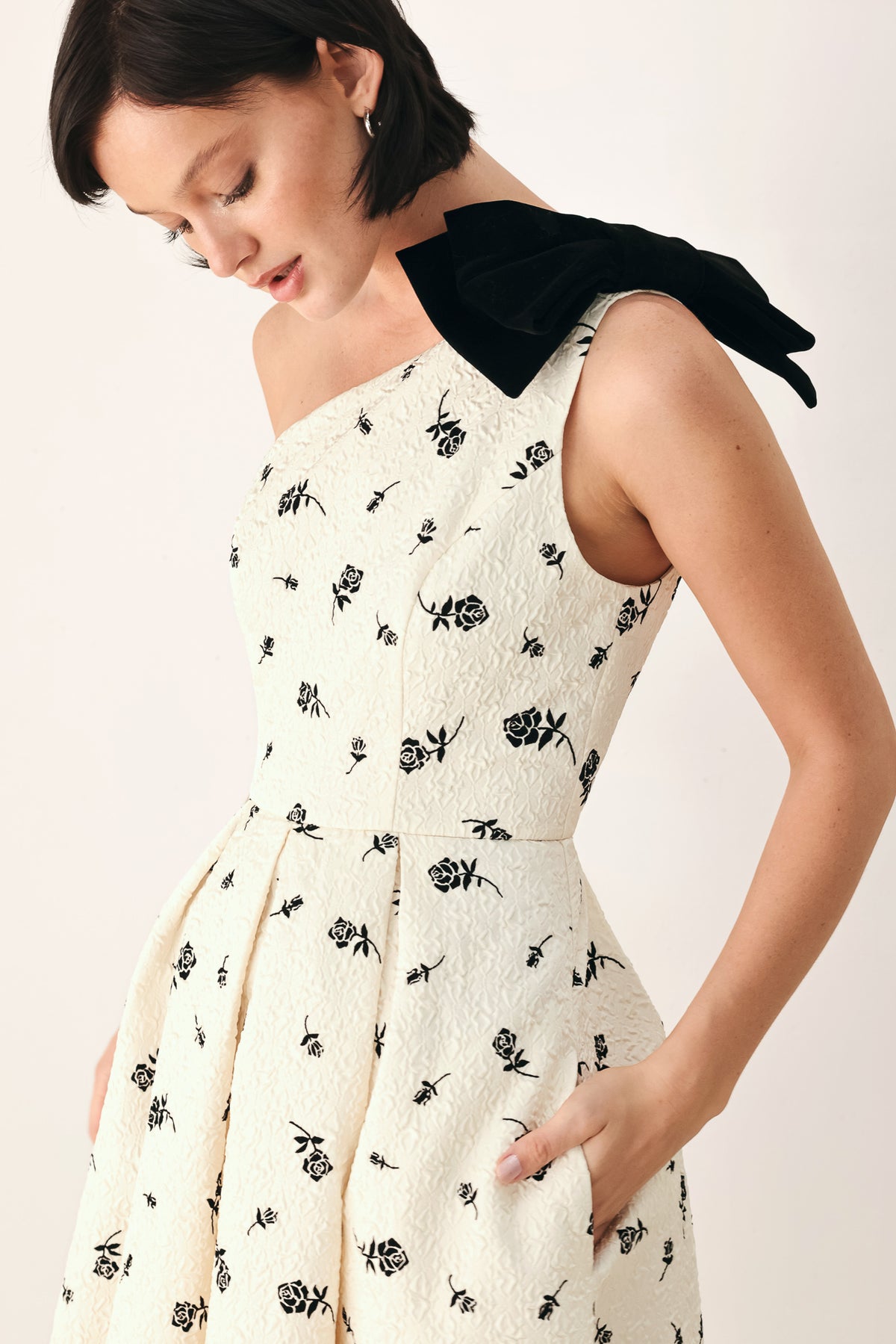 A woman models a one-shoulder midi dress with a black floral print on an off-white background, featuring a black fabric bow at the neckline | FREEMARKET