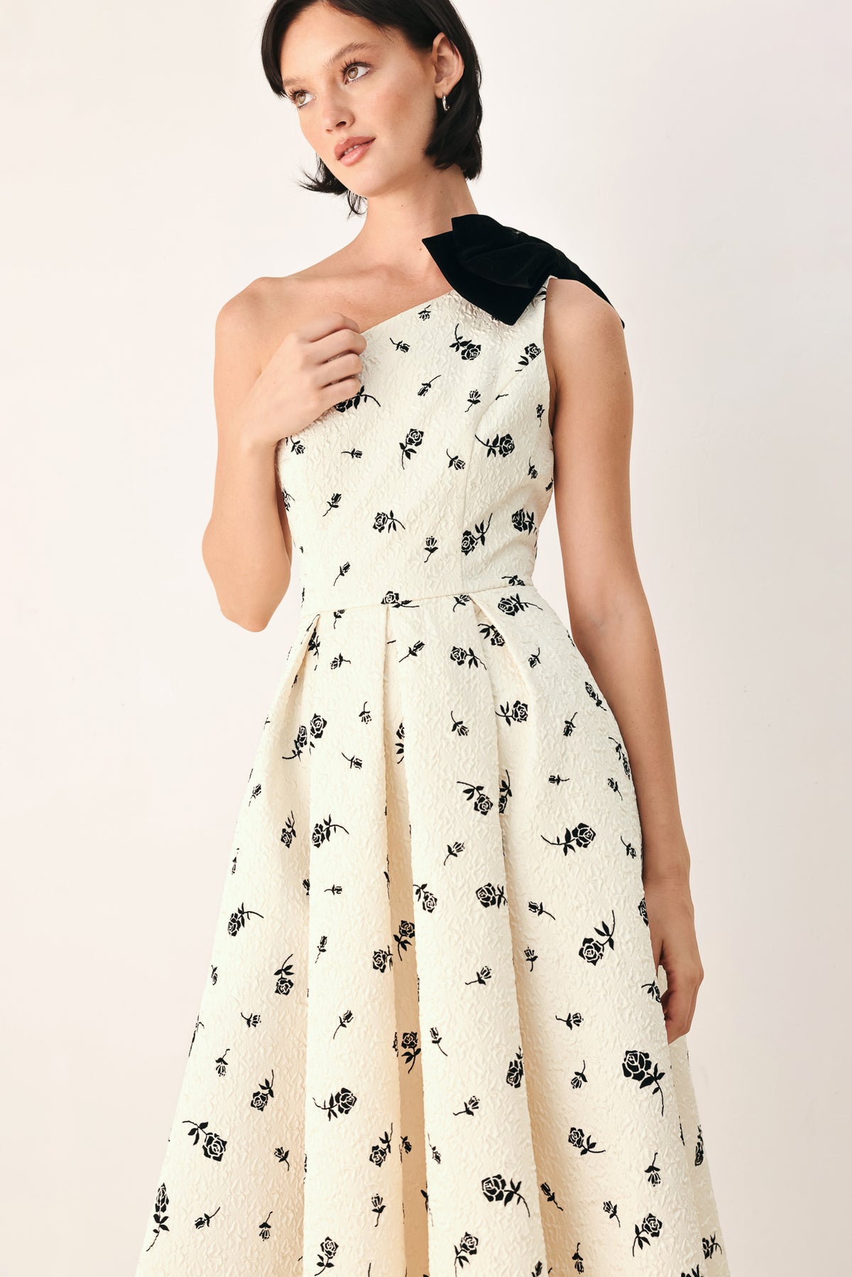 A woman models a one-shoulder midi dress with a black floral print on an off-white background, featuring a black fabric bow at the neckline | FREEMARKET