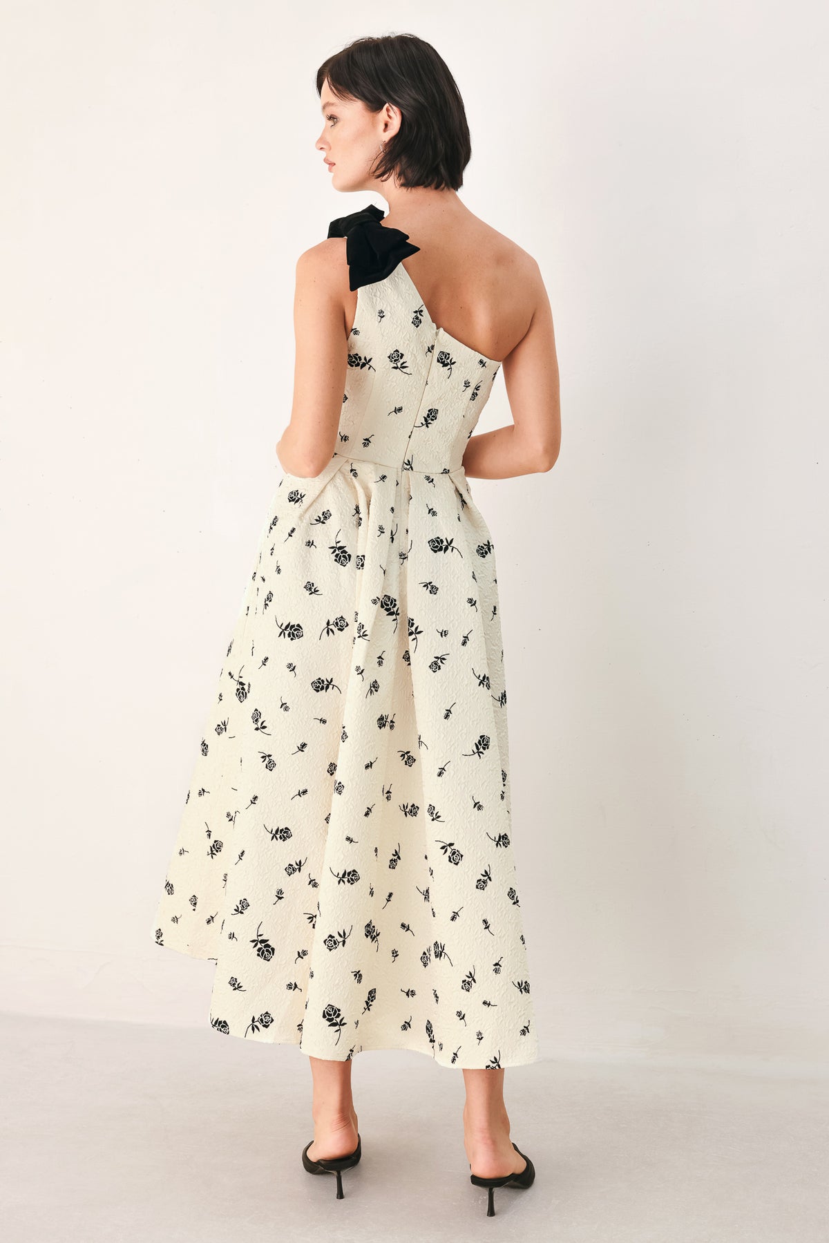 A woman models a one-shoulder midi dress with a black floral print on an off-white background, featuring a black fabric bow at the neckline | FREEMARKET