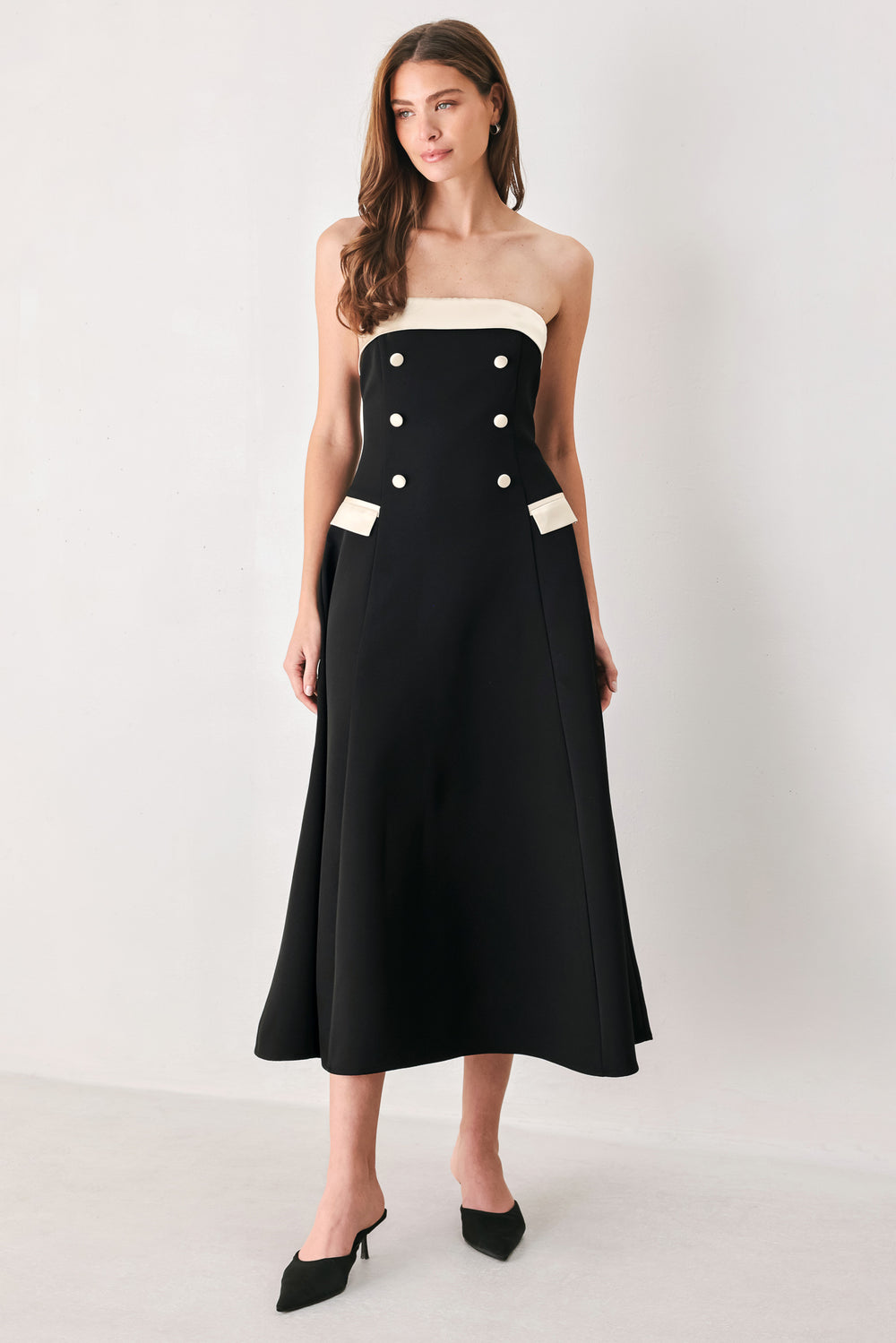Woman wearing a strapless black midi dress with cream strap across the strapless neckline, double breasted buttons, faux pockets | FREEMARKET