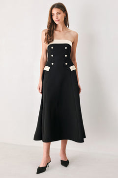 Woman wearing a strapless black midi dress with cream strap across the strapless neckline, double breasted buttons, faux pockets | FREEMARKET