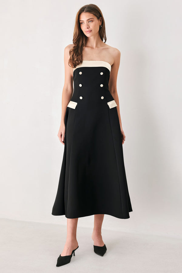 Woman wearing a strapless black midi dress with cream strap across the strapless neckline, double breasted buttons, faux pockets | FREEMARKET