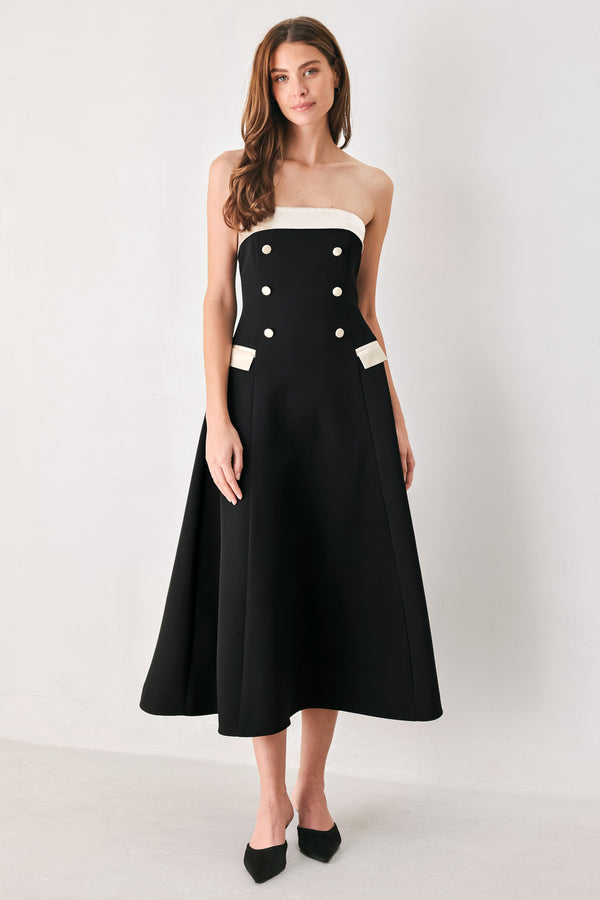 Woman wearing a strapless black midi dress with cream strap across the strapless neckline, double breasted buttons, faux pockets | FREEMARKET