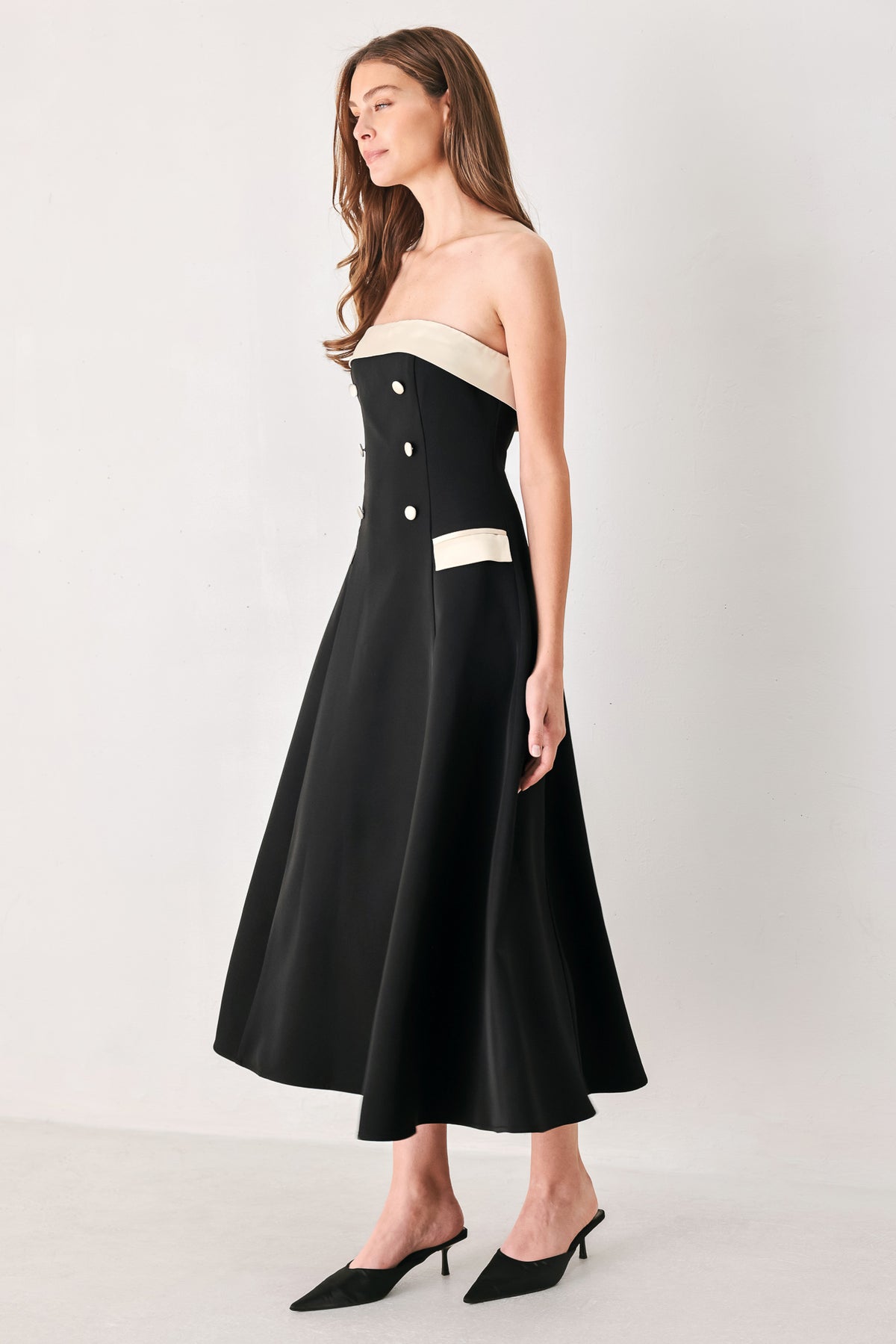 Woman wearing a strapless black midi dress with cream strap across the strapless neckline, double breasted buttons, faux pockets | FREEMARKET