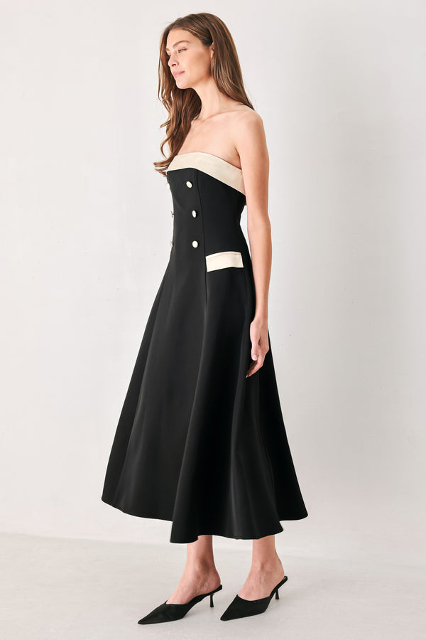 Woman wearing a strapless black midi dress with cream strap across the strapless neckline, double breasted buttons, faux pockets | FREEMARKET