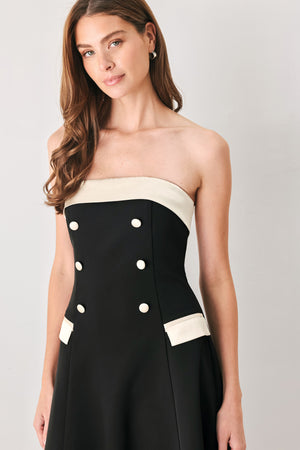 Woman wearing a strapless black midi dress with cream strap across the strapless neckline, double breasted buttons, faux pockets | FREEMARKET
