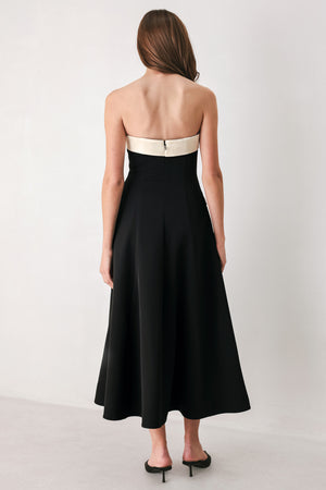 Woman wearing a strapless black midi dress with cream strap across the strapless neckline, double breasted buttons, faux pockets | FREEMARKET