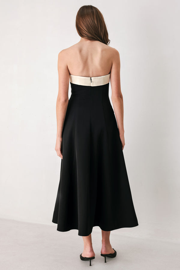 Woman wearing a strapless black midi dress with cream strap across the strapless neckline, double breasted buttons, faux pockets | FREEMARKET