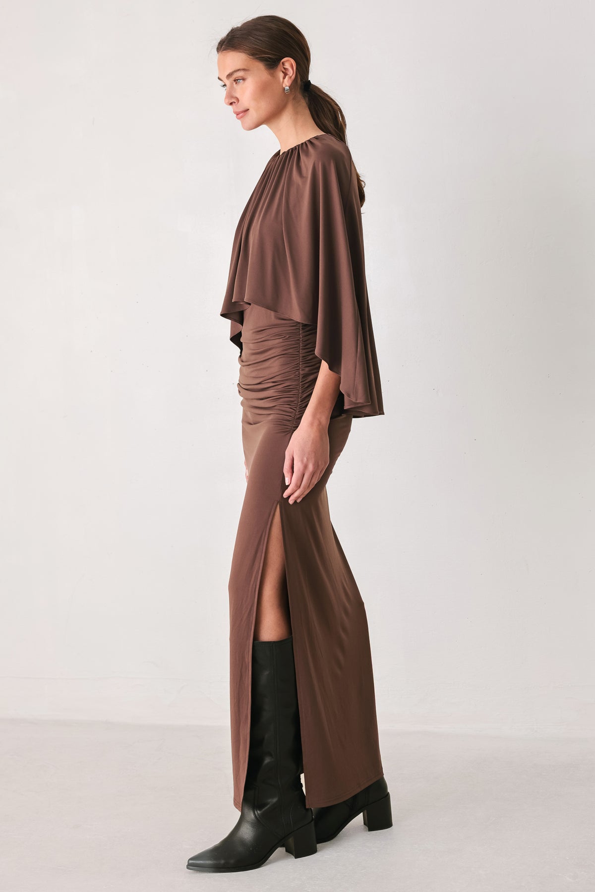 A woman models a brown mauve draped midi dress with a high neck, wide cape sleeves, ruched detailing at the waist, and a side slit | FREEMARKET