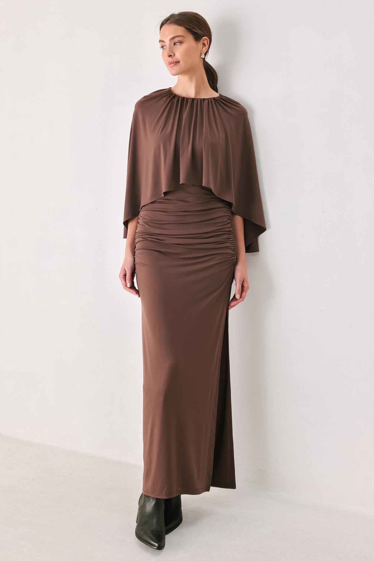 A woman models a brown mauve draped midi dress with a high neck, wide cape sleeves, ruched detailing at the waist, and a side slit | FREEMARKET