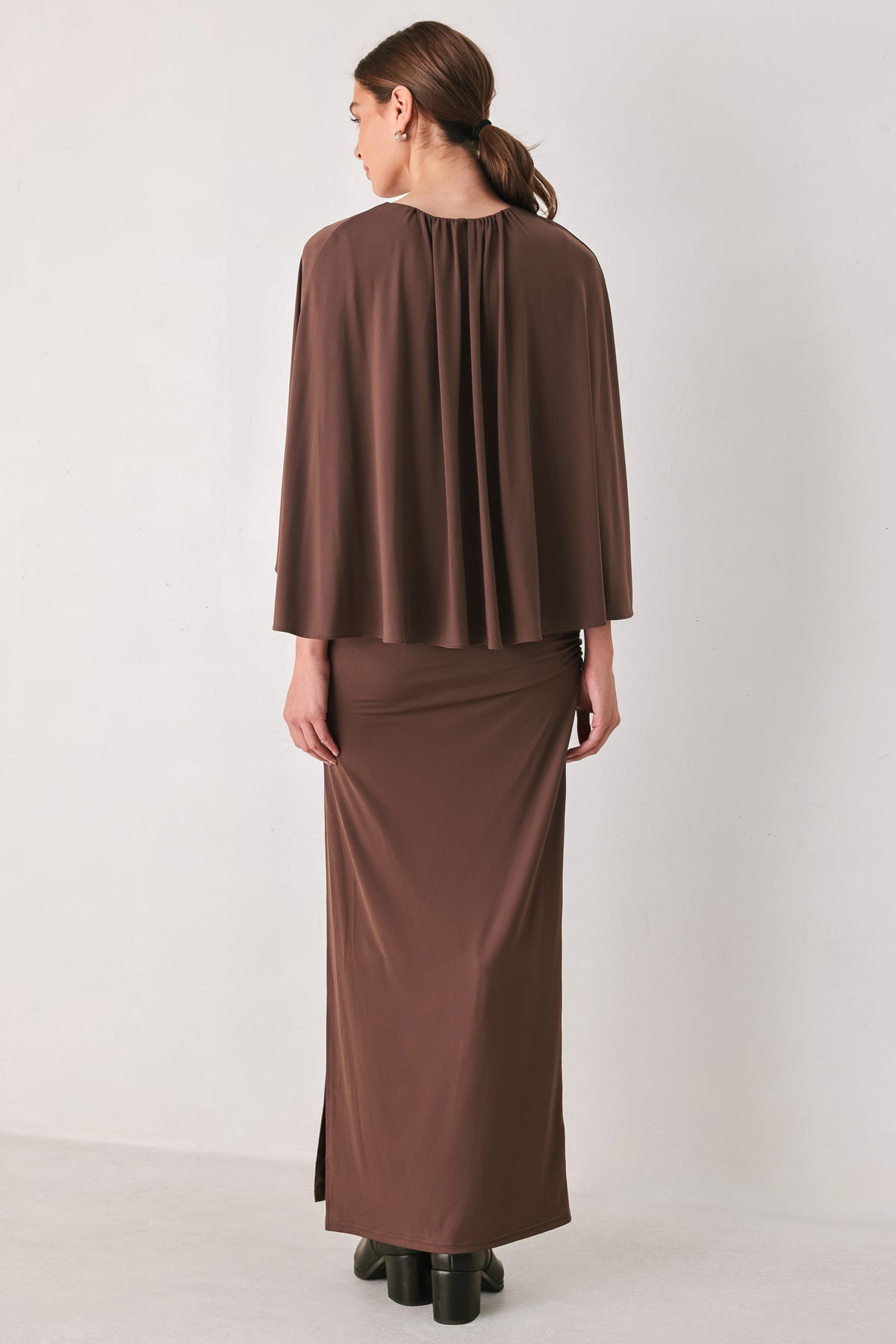A woman models a brown mauve draped midi dress with a high neck, wide cape sleeves, ruched detailing at the waist, and a side slit | FREEMARKET