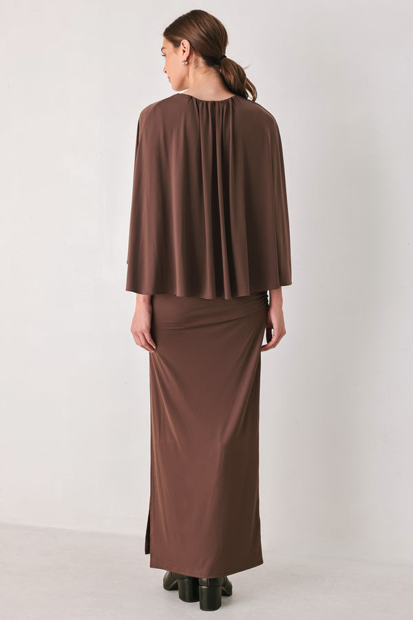A woman models a brown mauve draped midi dress with a high neck, wide cape sleeves, ruched detailing at the waist, and a side slit | FREEMARKET