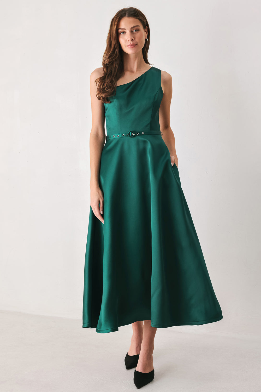 A woman models a sleeveless one-shoulder midi dress in emerald green satin, featuring a structured bodice, a thin waist belt, and a flared skirt | FREEMARKET