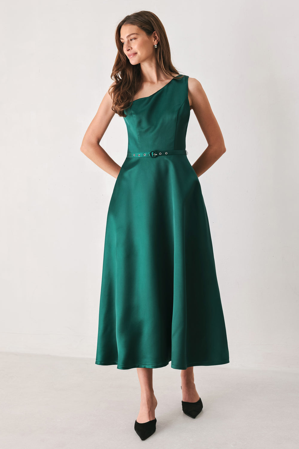A woman models a sleeveless one-shoulder midi dress in emerald green satin, featuring a structured bodice, a thin waist belt, and a flared skirt | FREEMARKET