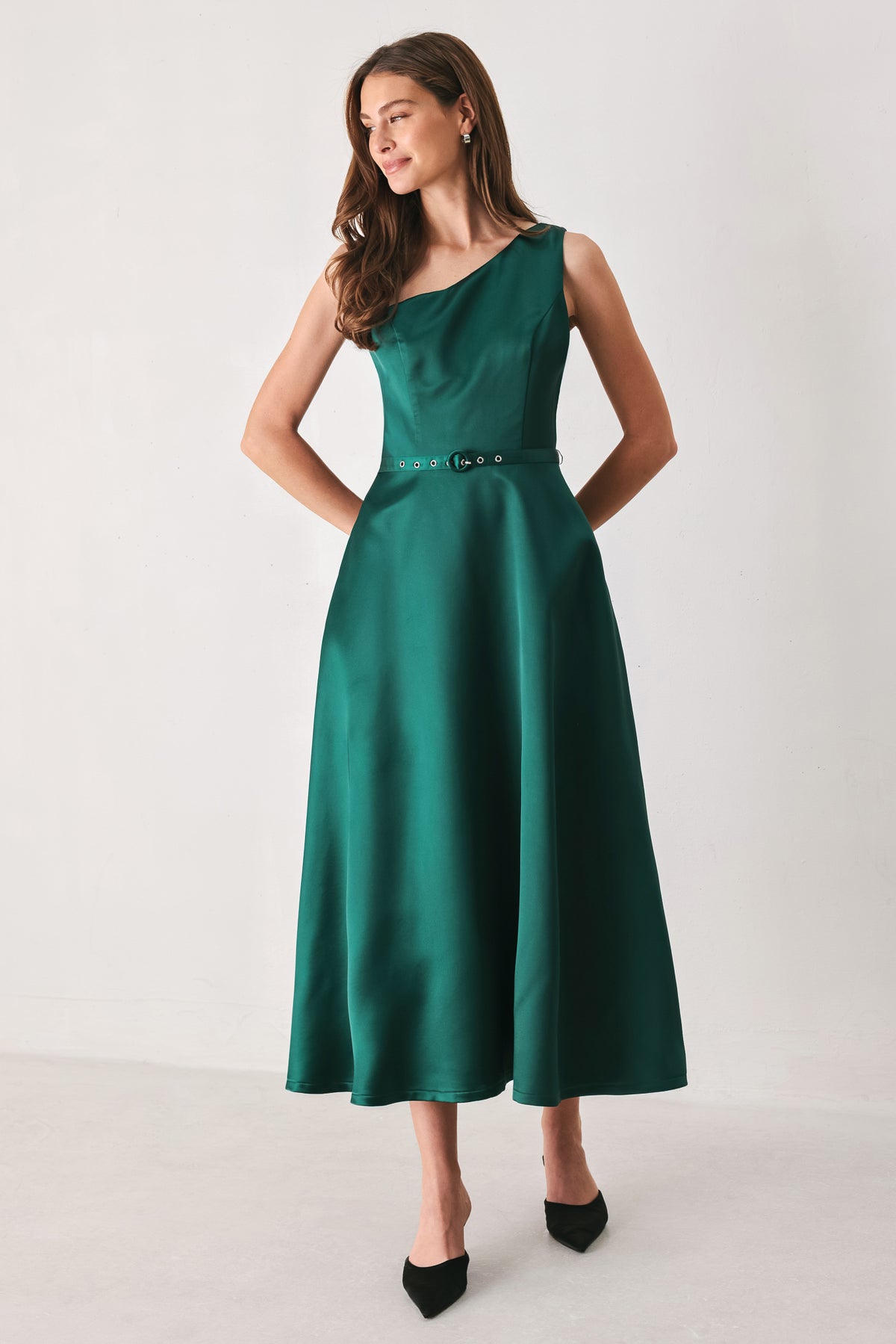 A woman models a sleeveless one-shoulder midi dress in emerald green satin, featuring a structured bodice, a thin waist belt, and a flared skirt | FREEMARKET