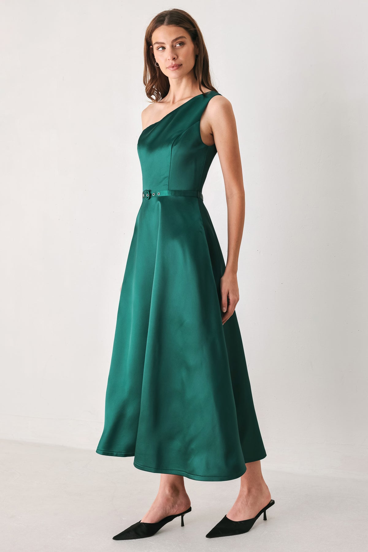A woman models a sleeveless one-shoulder midi dress in emerald green satin, featuring a structured bodice, a thin waist belt, and a flared skirt | FREEMARKET