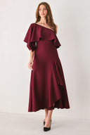 Woman wearing a burgundy midi dress with with an asymmetrical neckline with a large ruffle and a ruffle along the leg slit | FREEMARKET
