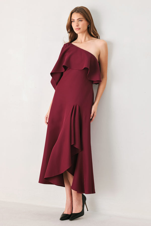Woman wearing a burgundy midi dress with with an asymmetrical neckline with a large ruffle and a ruffle along the leg slit | FREEMARKET