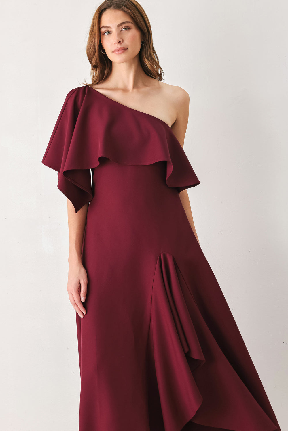 Woman wearing a burgundy midi dress with with an asymmetrical neckline with a large ruffle and a ruffle along the leg slit | FREEMARKET