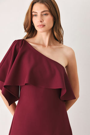 Woman wearing a burgundy midi dress with with an asymmetrical neckline with a large ruffle and a ruffle along the leg slit | FREEMARKET