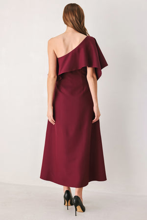 Woman wearing a burgundy midi dress with with an asymmetrical neckline with a large ruffle and a ruffle along the leg slit | FREEMARKET