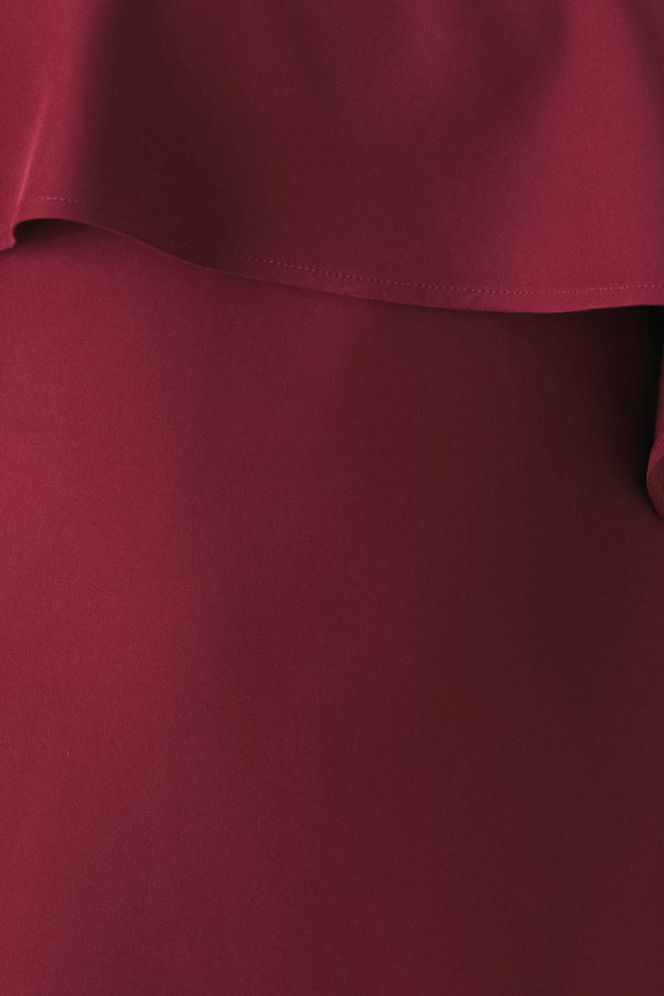 Woman wearing a burgundy midi dress with with an asymmetrical neckline with a large ruffle and a ruffle along the leg slit | FREEMARKET