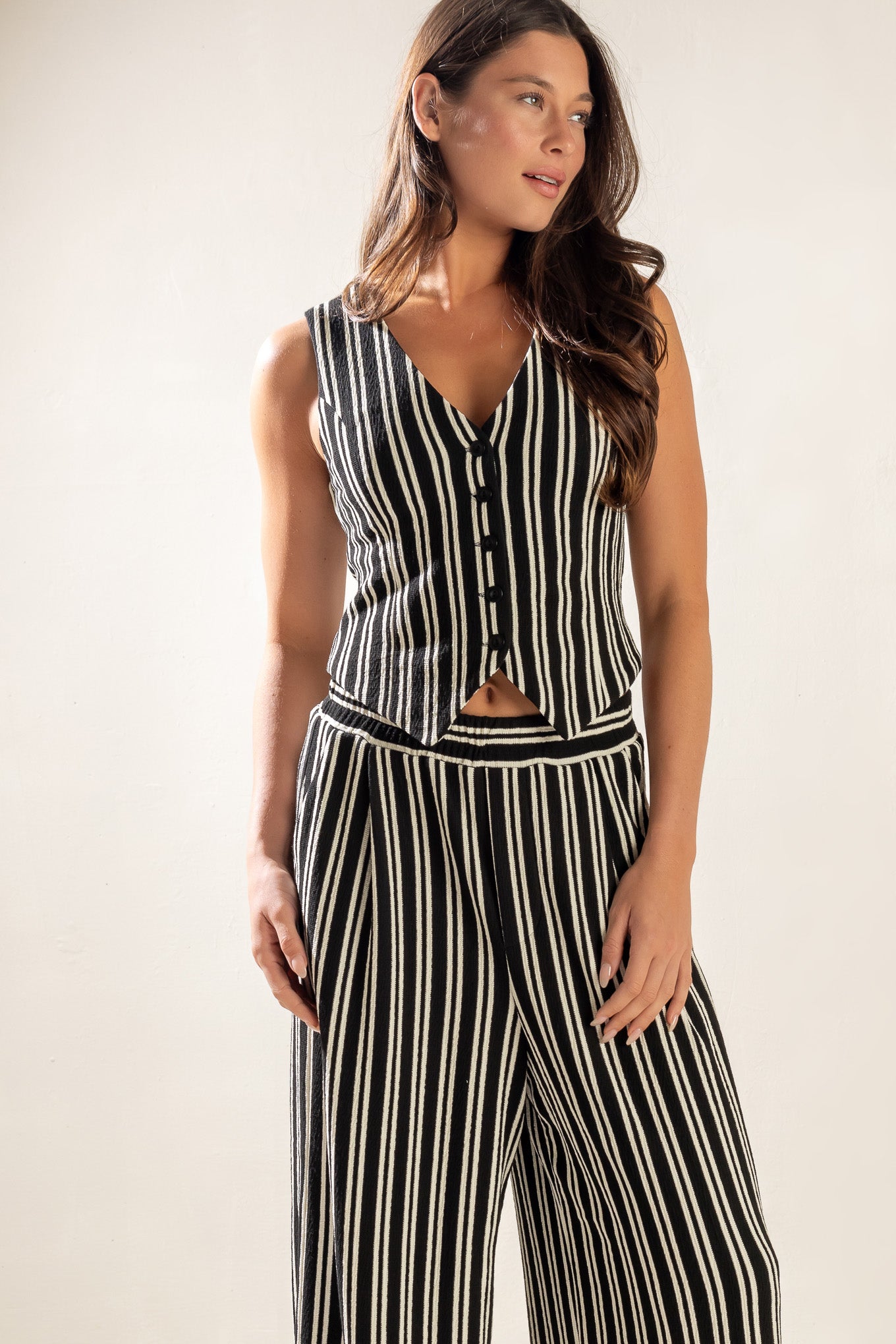 A striped black and white woven vest featuring sleeveless and front button closure.