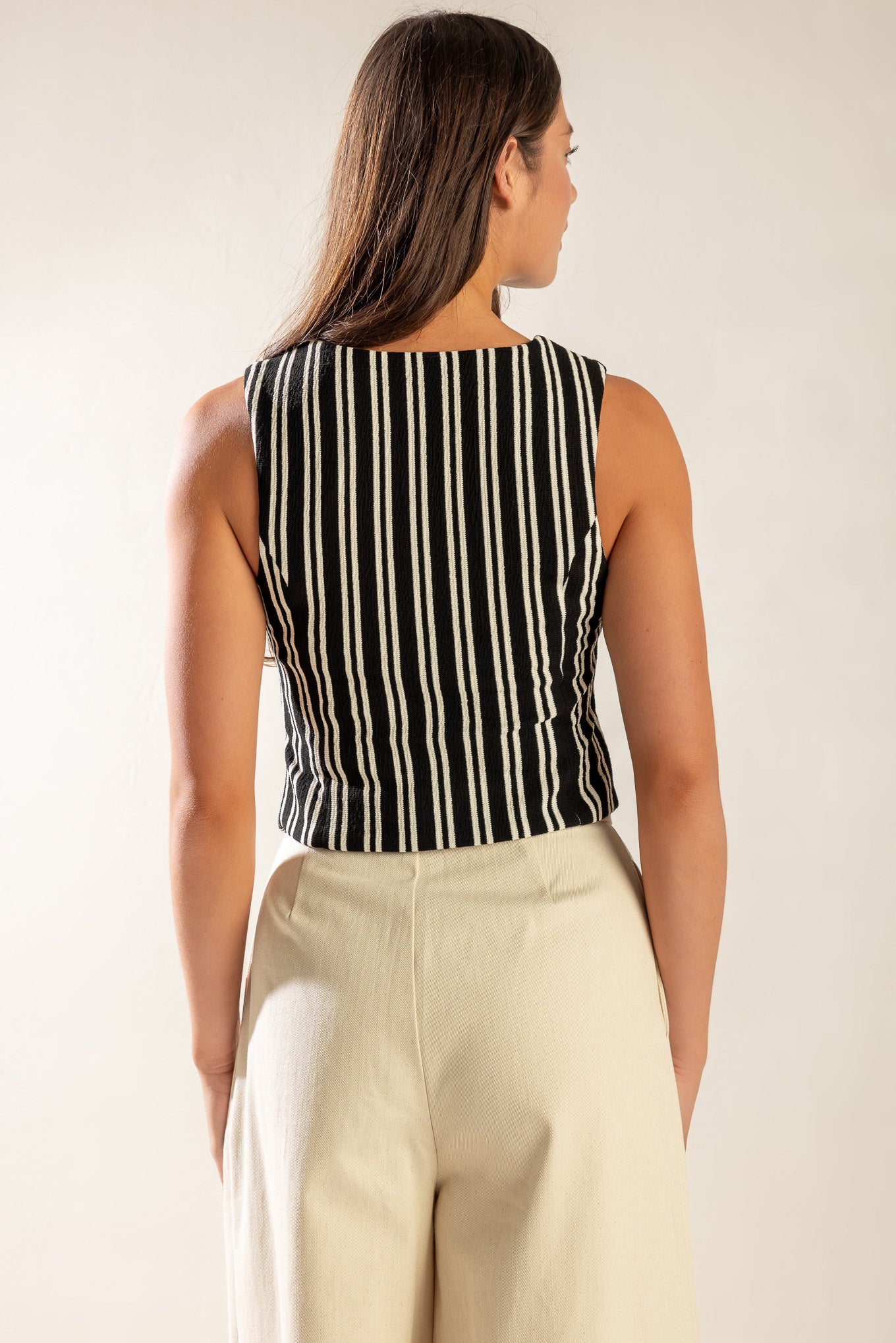 A striped black and white woven vest featuring sleeveless and front button closure.