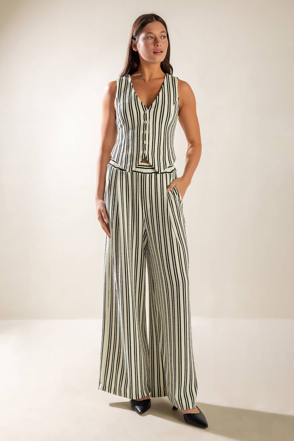 A striped black and white woven vest featuring sleeveless and front button closure.