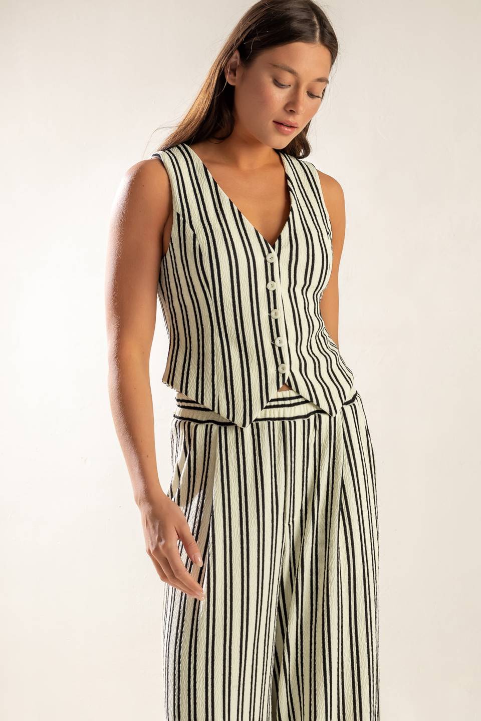 A striped black and white woven vest featuring sleeveless and front button closure.